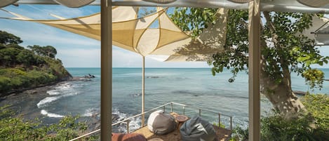 A seaside terrace with a view of the ocean, featuring a seating area with cushions and a table.