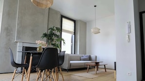 Ett modernt vardagsrum med en matplats, inrett med en soffa, ett soffbord, ett matbord med stolar, en stor krukväxt och en hängande lampa.