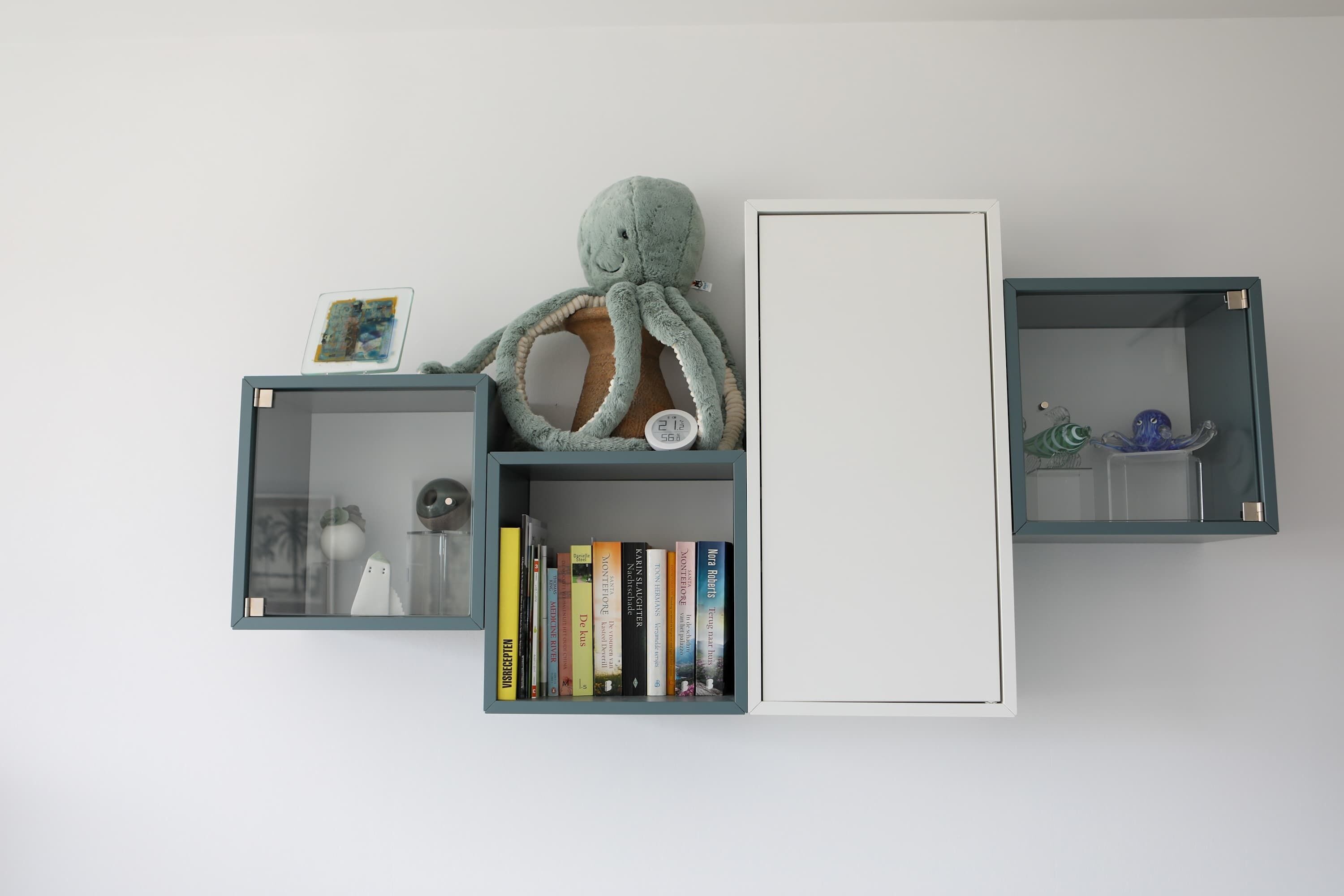 Drei Wandregale mit Büchern, einem weichen Plüsch-Tintenfisch und Dekorationselementen.