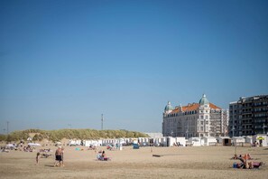 A beach with tents and umbrellas, a large building with a dome, and a sandy area with people. - Seaside Retreat: Modern Waterfront Apt Near Bruges (Bruges)