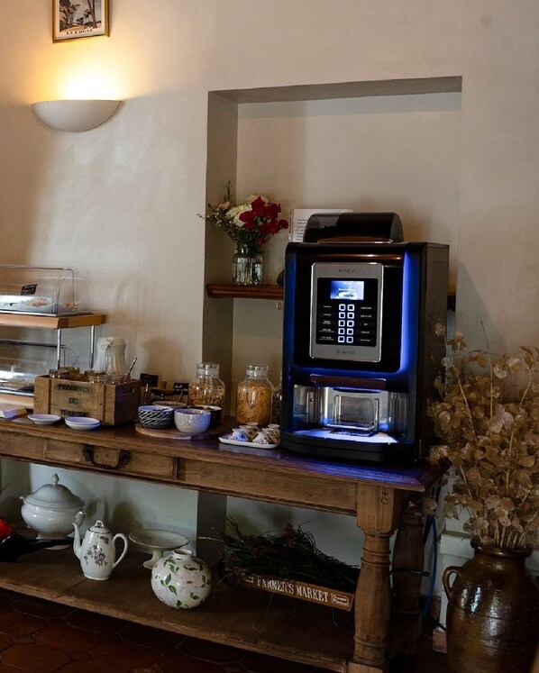Een keukenhoek met een koffieapparaat, potten met kruiden en een vintage theepot op een houten aanrecht.