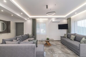 Ein modernes Wohnzimmer mit grauen Sofas, einem Couchtisch und einem an der Wand montierten Fernseher.