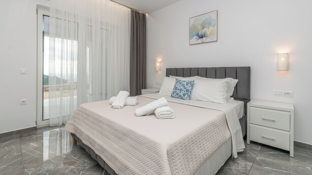 Et moderne hotelværelse med en stor seng, et natbord, en vægmonteret lampe og udsigt gennem en glasdør.