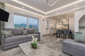 Ein modernes Wohnzimmer mit einem grauen Sofa, einem Couchtisch mit Pflanze und Blick auf die Berge durch große Fenster.