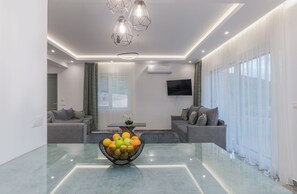 Ein modernes Wohnzimmer mit einem Glastisch, grauen Sofas und einer Obstschale.