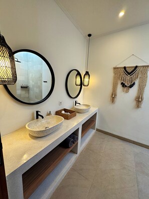 Ein modernes Badezimmer mit zwei runden Spiegeln, einem Haubenwaschbecken und einer hängenden Lampenschirm aus Makramee.