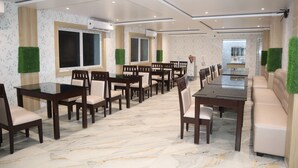 A spacious dining area with a long table and multiple chairs, surrounded by walls with floral wallpaper and green artificial grass accents. - New Beach Resort (Brahmagiri)