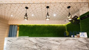 A reception area with a marble counter, green artificial grass wall, and geometric ceiling design. - New Beach Resort (Brahmagiri)