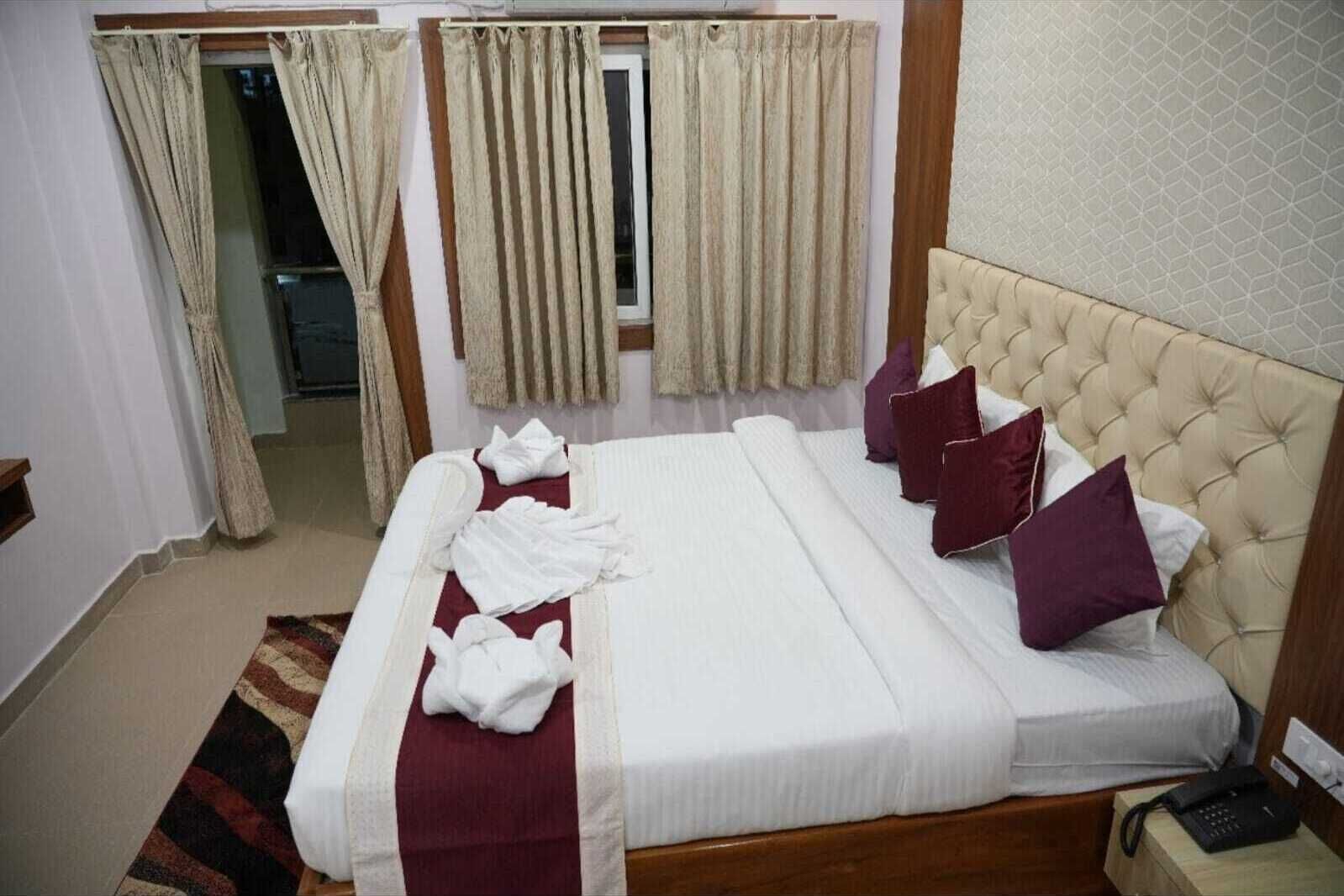 Habitación de hotel con una cama grande, cortinas color beige, cabecero de madera y teléfono en la mesita de noche.
