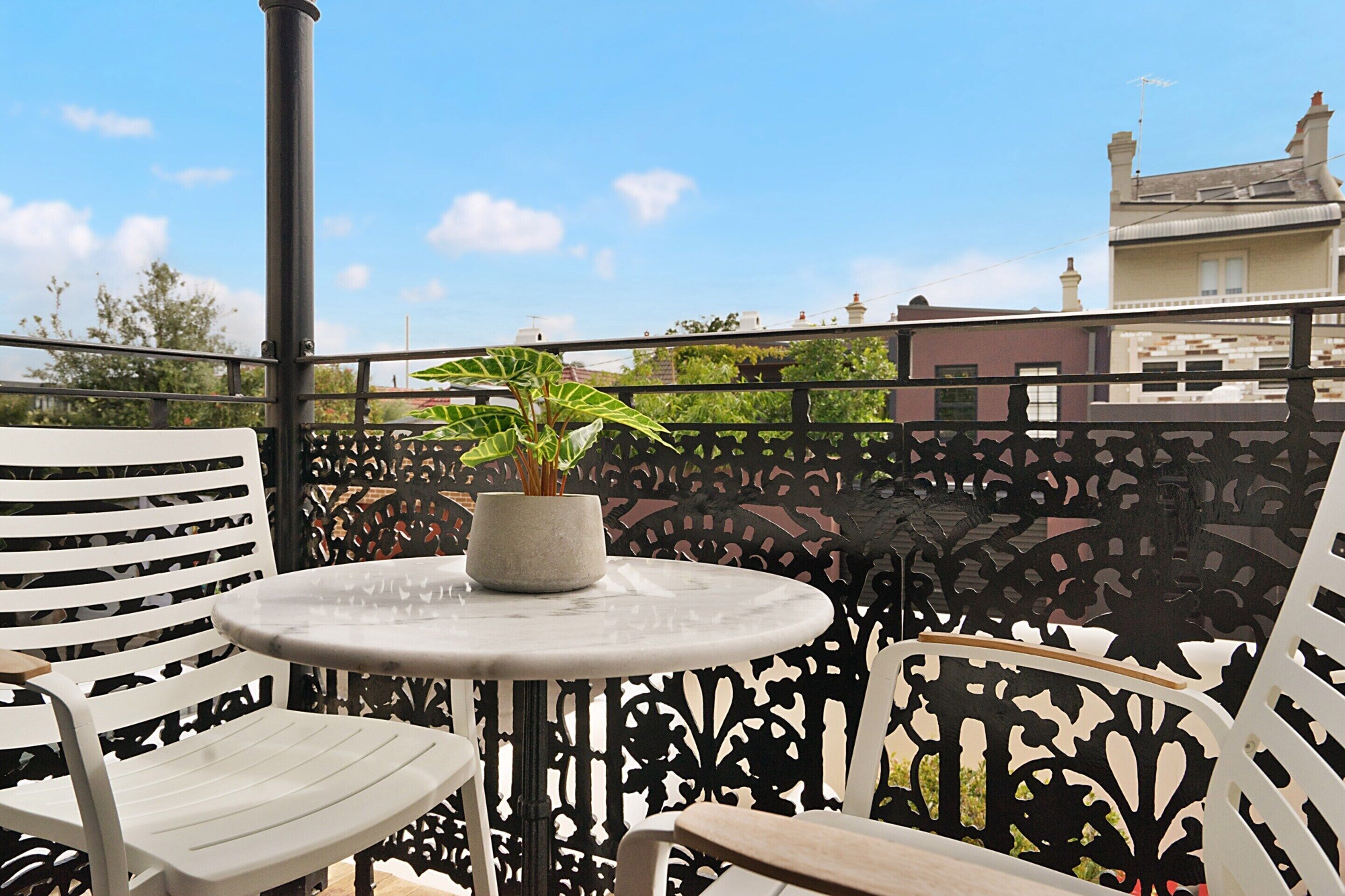 Un balcon avec une table ronde et deux chaises, un pot de fleurs et une clôture décorative en métal.