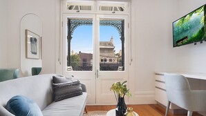 A living room with a sofa, a coffee table, a TV, and a view through a door. - Cozy Studio With Balcony in Unbeatable Location (Sydney)