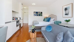 A modern apartment with a kitchenette, a living area with a sofa and a bed, and a dining table. - Cozy Studio With Balcony in Unbeatable Location (Sydney)