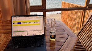 Ein Laptop auf einem Holztisch mit einer Corona Extra Bierflasche, mit Blick auf einen Strand.