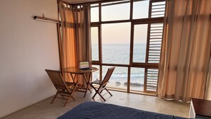 Ein Zimmer mit einem Bett, einem Tisch und zwei Stühlen sowie Meerblick durch große Fenster.