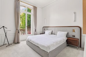 Een slaapkamer met een groot bed, een nachtkastje, een wandlamp en een raam met gordijnen.