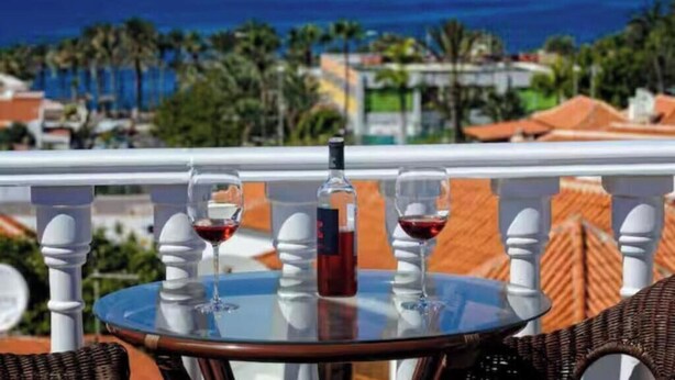 Ein Tisch mit zwei Weingläsern und einer Flasche auf einem Balkon mit Blick auf die Küste.