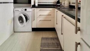 Eine kompakte Küche mit Waschmaschine, Mikrowelle, Backofen und einem kleinen Fenster.
