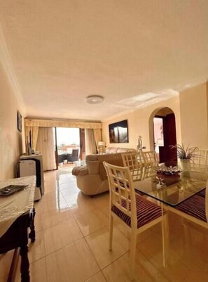A dining area with a glass table, chairs, and a sofa in the background. - Apartment with Terrace in Playa de las Americas - Swimming Pool and Ideal Location (Arona)