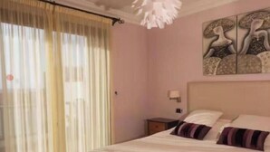Ein Schlafzimmer mit einem Bett, einem Nachttisch, einer Wandlampe und einem Fenster mit durchsichtigen Vorhängen.