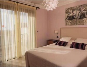 A bedroom with a bed, a nightstand, a wall-mounted lamp, and a window with sheer curtains. - Apartment with Terrace in Playa de las Americas - Swimming Pool and Ideal Location (Arona)