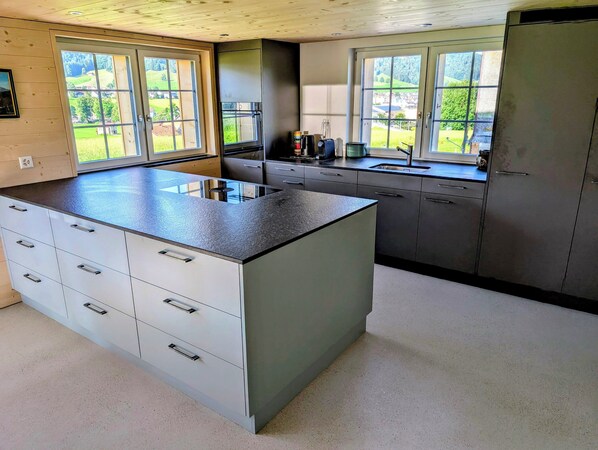 A modern kitchen with a central island, large windows, and a view of the outdoors.
