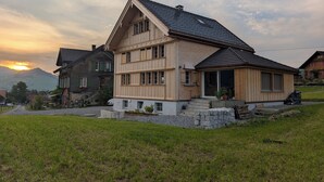 A two-story wooden house with a sloped roof, a front porch, and a stone foundation.