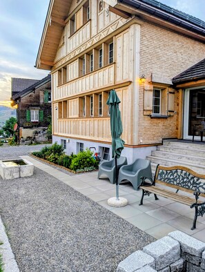 A wooden building with a balcony, outdoor seating, and a stone fountain. - Panoramic Views & Appenzell Charm: Your Spacious Retreat (Appenzell)