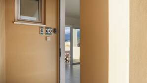 Corredor com uma porta que dá para uma varanda. Há o número 460 na parede, e uma janela acima da porta.