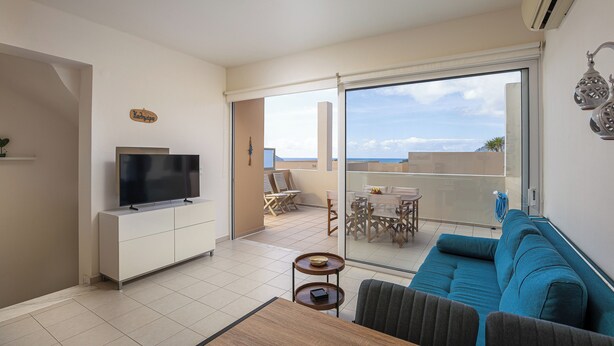 Sala de estar moderna com televisão de tela plana, sofá, mesa de centro e varanda com mesa e cadeiras.