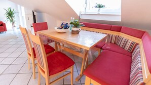 Zona pranzo con tavolo in legno e sedie imbottite rosse. Si vede una finestra con vista all'esterno.