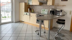 Una cucina con piano cottura, forno a microonde e macchina da caffè. Una finestra offre vista sugli edifici esterni.