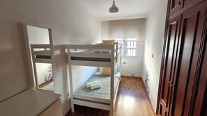 A bunk bed room with a wooden floor, a white dresser, a window with bars, and a door with a wooden frame. - Apartment 50 meters from the sea (La Cala del Moral)