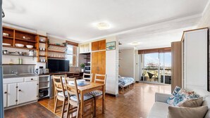 A compact apartment with a kitchenette, dining area, and a balcony with a city view. - River Vistas - Fremantle Port Views (North Fremantle)