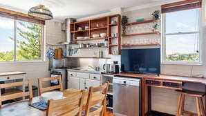 A modern kitchen with a dining area, wooden cabinets, a dishwasher, and a large window providing a view of the outdoors. - River Vistas - Fremantle Port Views (North Fremantle)