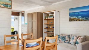 A dining area with a wooden table and chairs, a sofa with patterned cushions, and a bookshelf with decorative items. - River Vistas - Fremantle Port Views (North Fremantle)