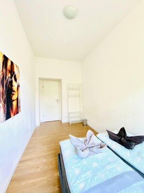 A hotel room with a wooden floor, a bed with a patterned bedspread, a wall-mounted shelf, and a door leading to another room. - Ideal 3BR Apartment Near Stammersdorf (Vienna)