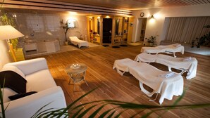 Un área de spa con suelo de madera, sillones blancos, una pequeña mesa con velas y un mostrador de recepción con espejo.