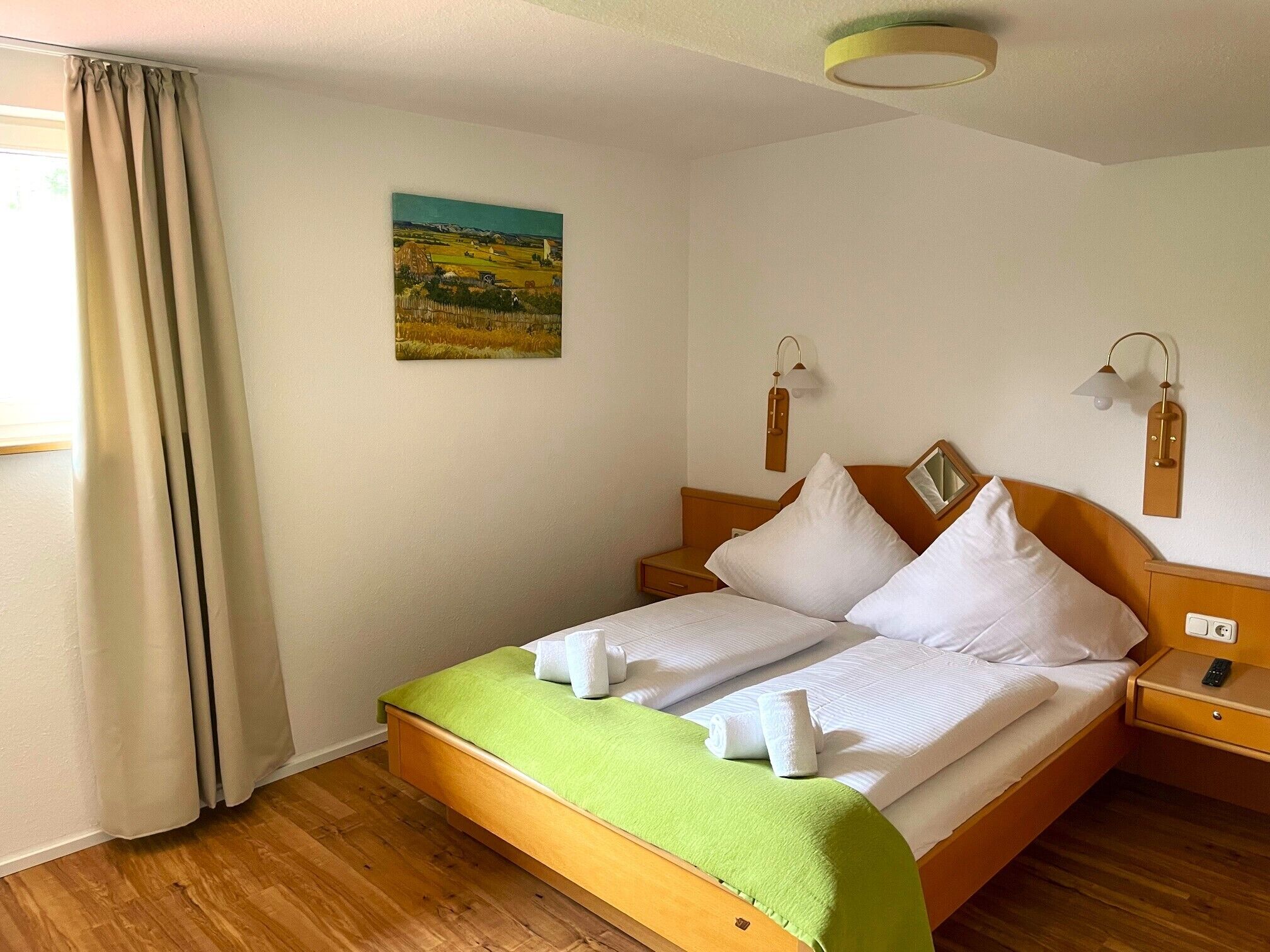 A neatly made bed with a green blanket, wooden headboard, two bedside tables with lamps, and a painting on the wall.