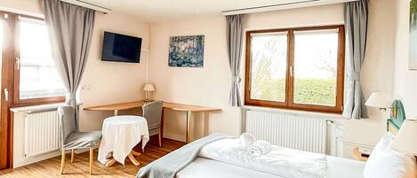 A hotel room with a bed, a desk, a chair, a TV, and a window with curtains.