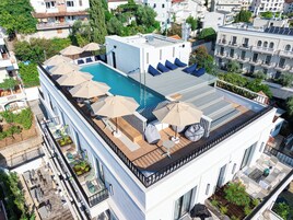 Área de piscina en la azotea con varias sillas de descanso y sombrillas, rodeada por un edificio blanco con balcones.