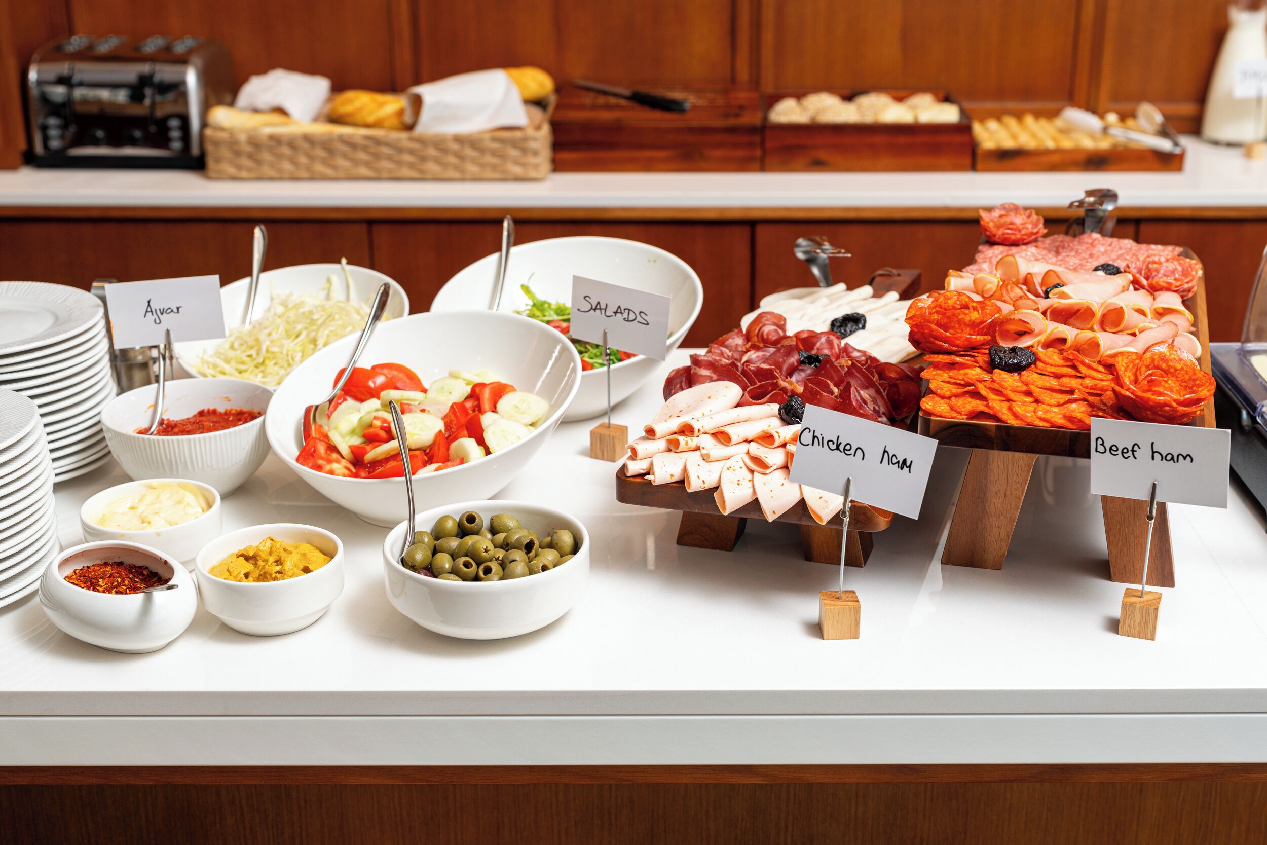 Un bufé con diversas opciones de comida, incluyendo ensaladas, jamón de pollo y jamón de res.