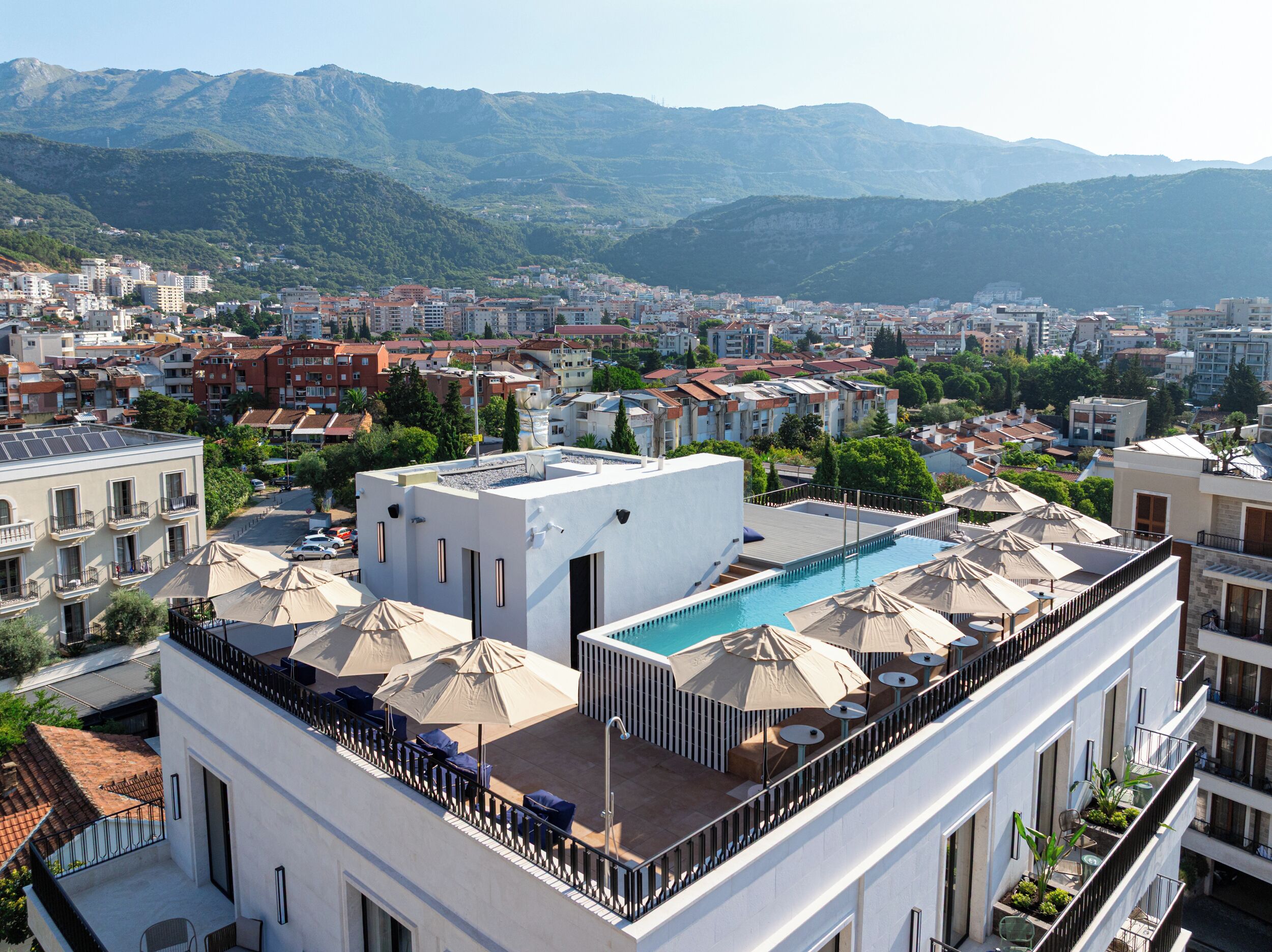 Un área de piscina en la azotea con varios sombrillas y asientos, con vistas a un paisaje urbano y montañas al fondo.