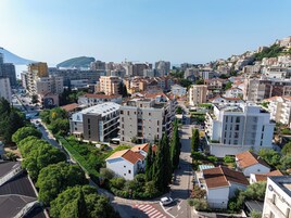 Zona residencial con edificios de varios pisos, una calle con coches y una colina al fondo.