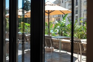 An outdoor seating area with tables and chairs, surrounded by greenery and umbrellas.