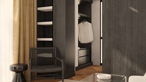 A modern room with a wooden floor, a black chair, a white sofa, a glass coffee table, and a wardrobe with a hanging rack. - Hotel Madeira (Budva)