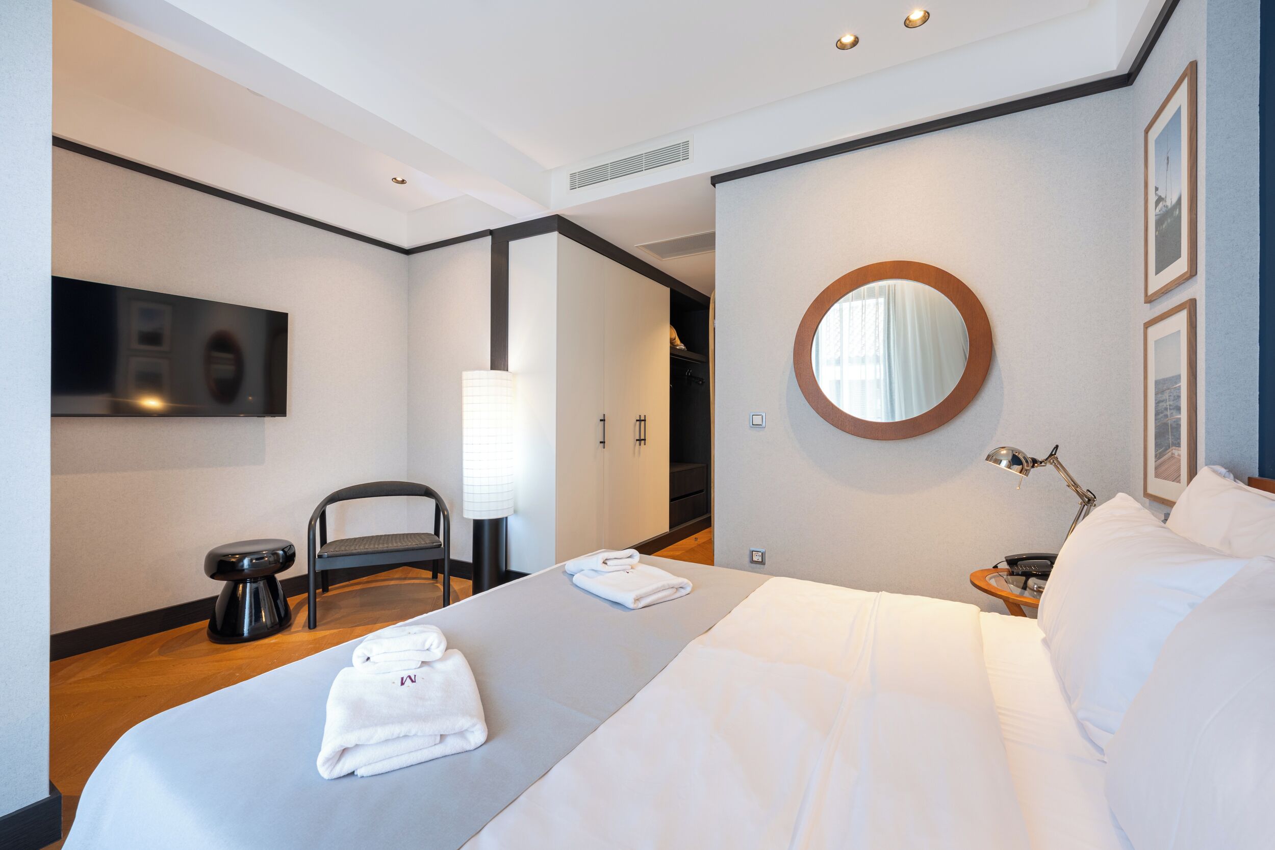 A modern hotel room with a bed, a chair, a desk, a lamp, a mirror, and a television.
