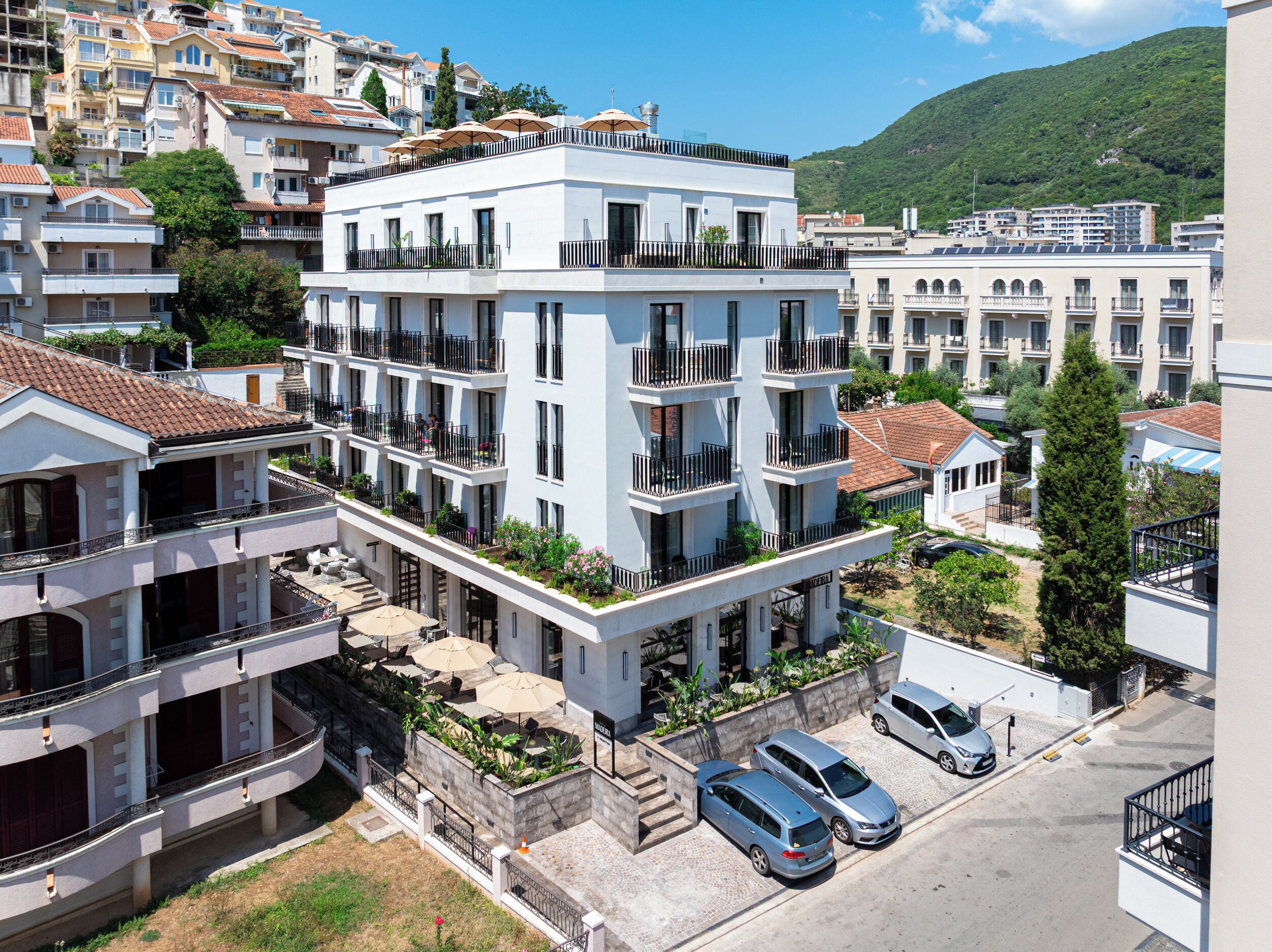 Un hotel de varios pisos con balcones, mobiliario exterior y zona de estacionamiento.