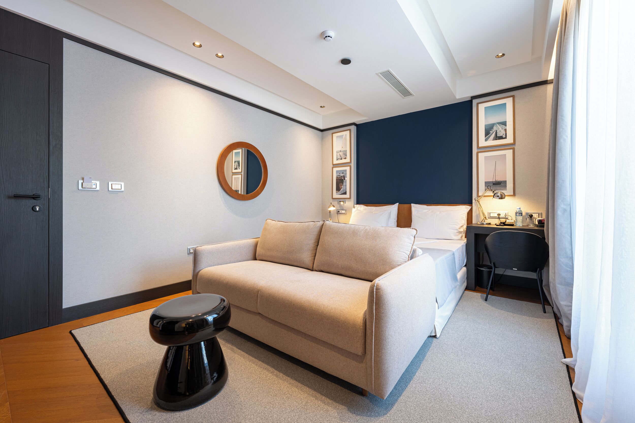 Una habitación de hotel moderna con un sofá, una pequeña mesa redonda, un escritorio con una silla y una cama.