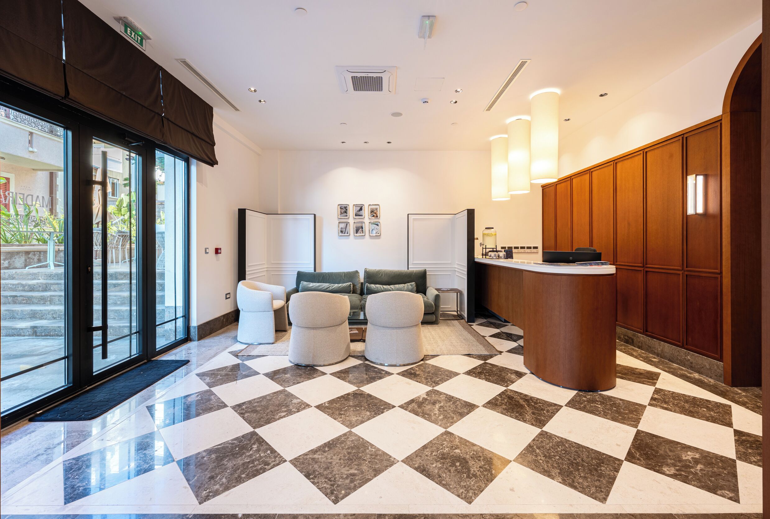 Um saguão de hotel com piso xadrez, área de estar, balcão de recepção e vista para o exterior.