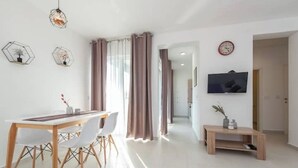 A modern living room with a dining area, a TV mounted on the wall, and a hallway leading to another room. - Villa Isola apartments 2 (Novalja)